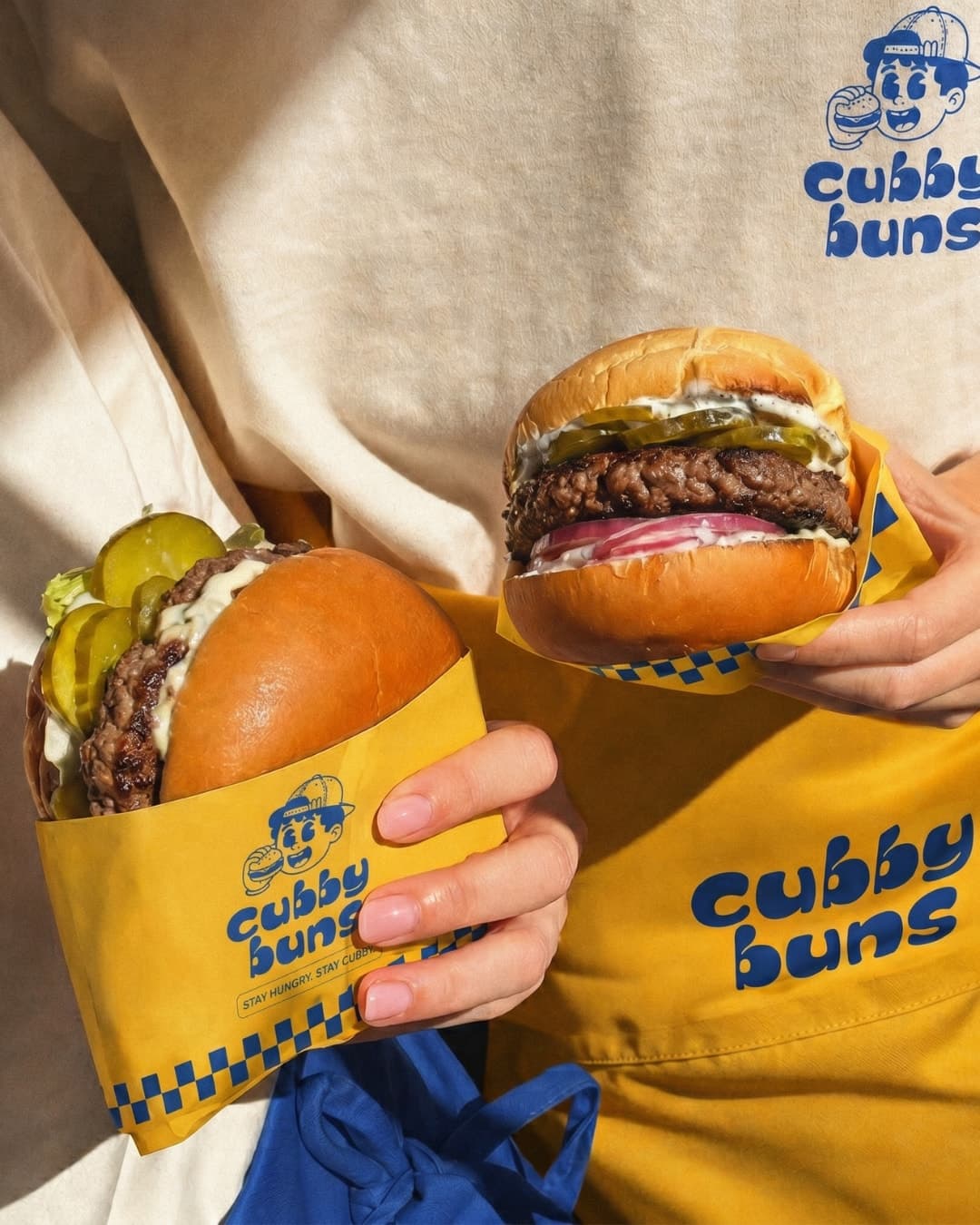 Two burgers in yellow Cubby Buns wraps held against an apron