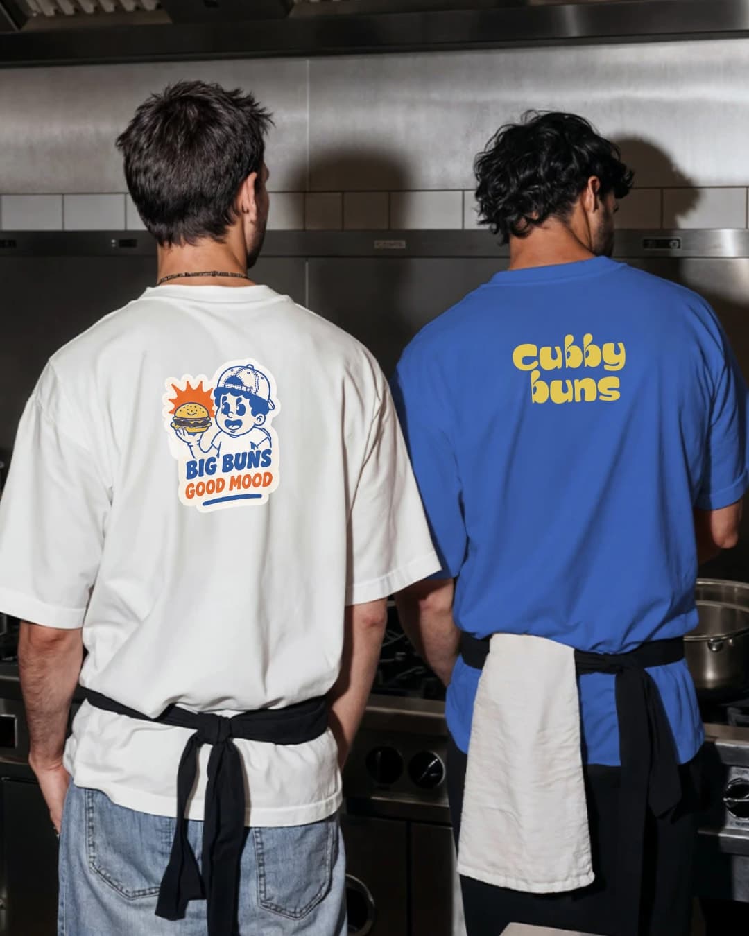 Two staff in Cubby Buns tees in the kitchen, seen from behind