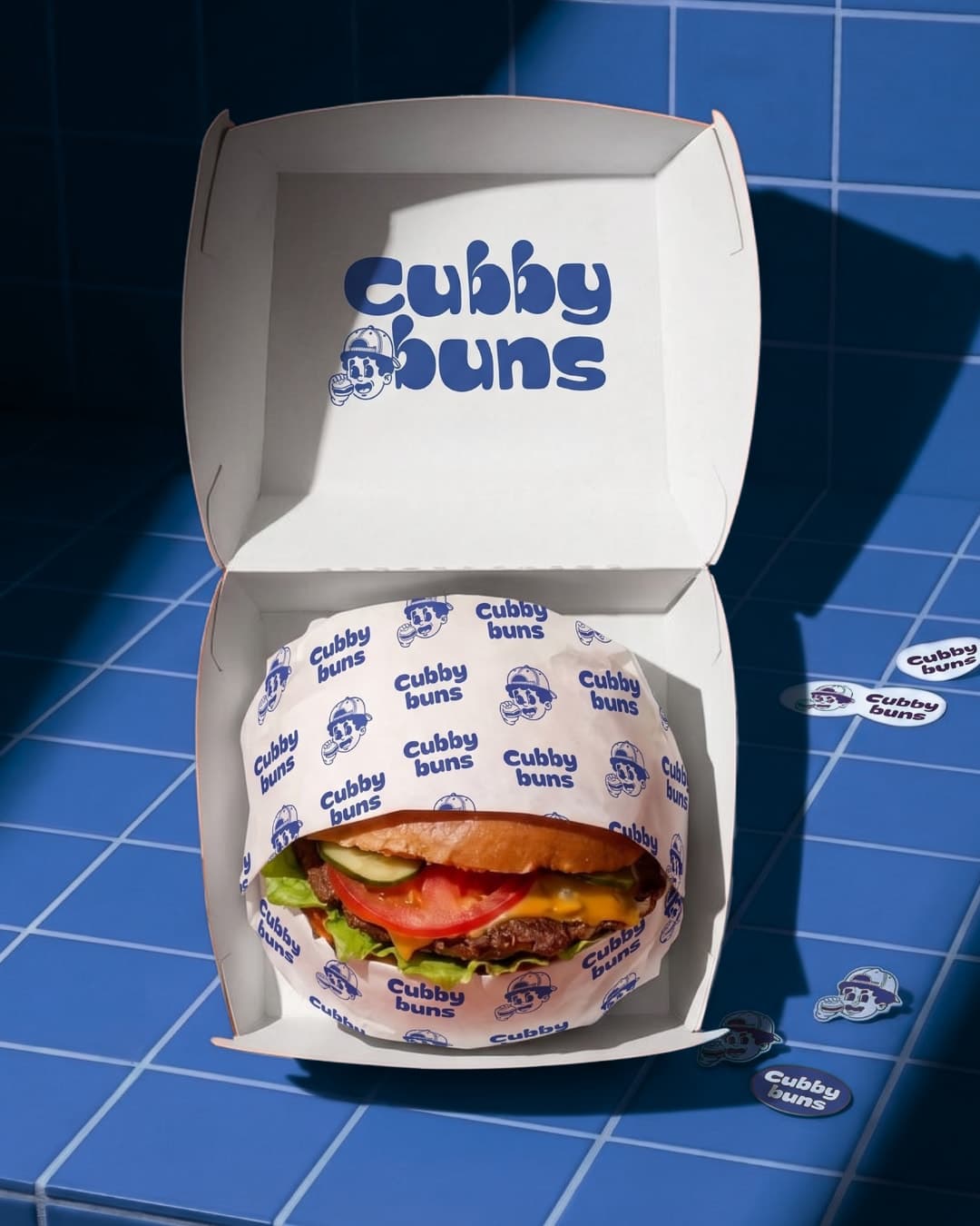 Open Cubby Buns box with a wrapped burger on blue tiles