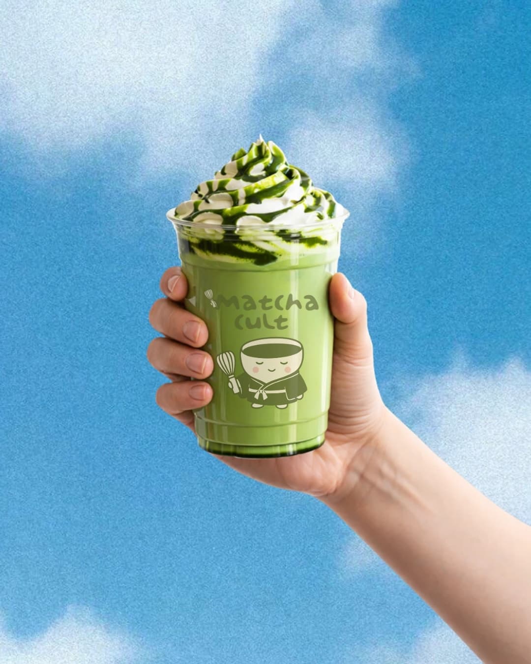 Hand holding a whipped iced matcha cup against a blue sky